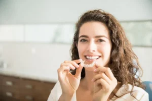 Woman smiling while holding a clear dental aligner between her fingers.