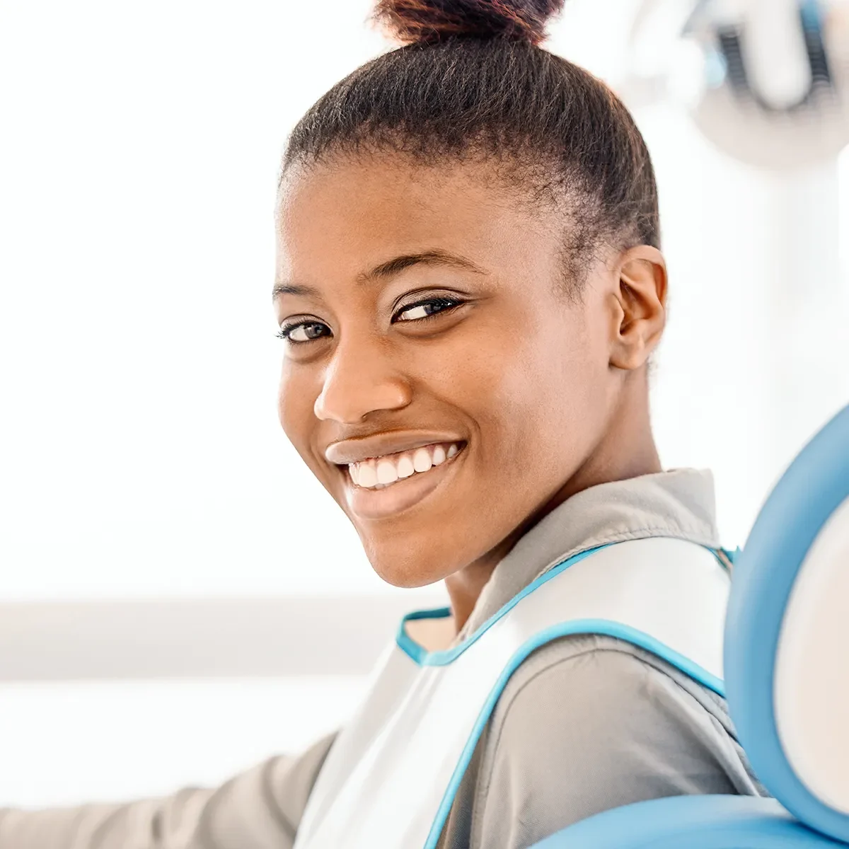 A woman with a bright smile sits in a dental chair, after receiving dental bridges