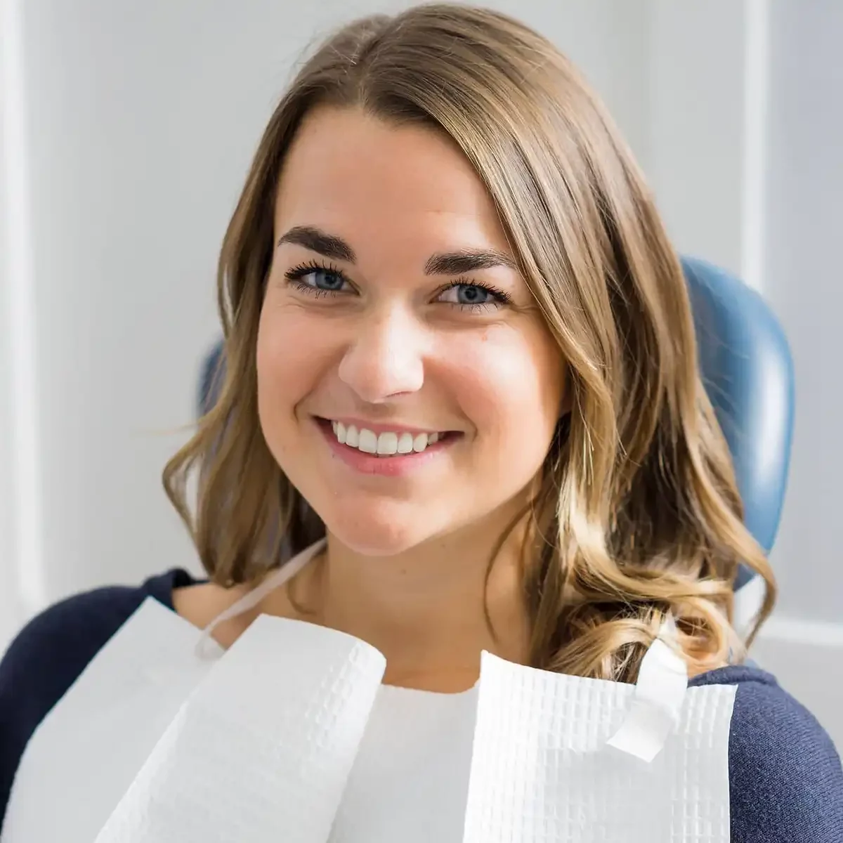 A woman with a bright smile sits in a dental chair, after receiving dental bridges