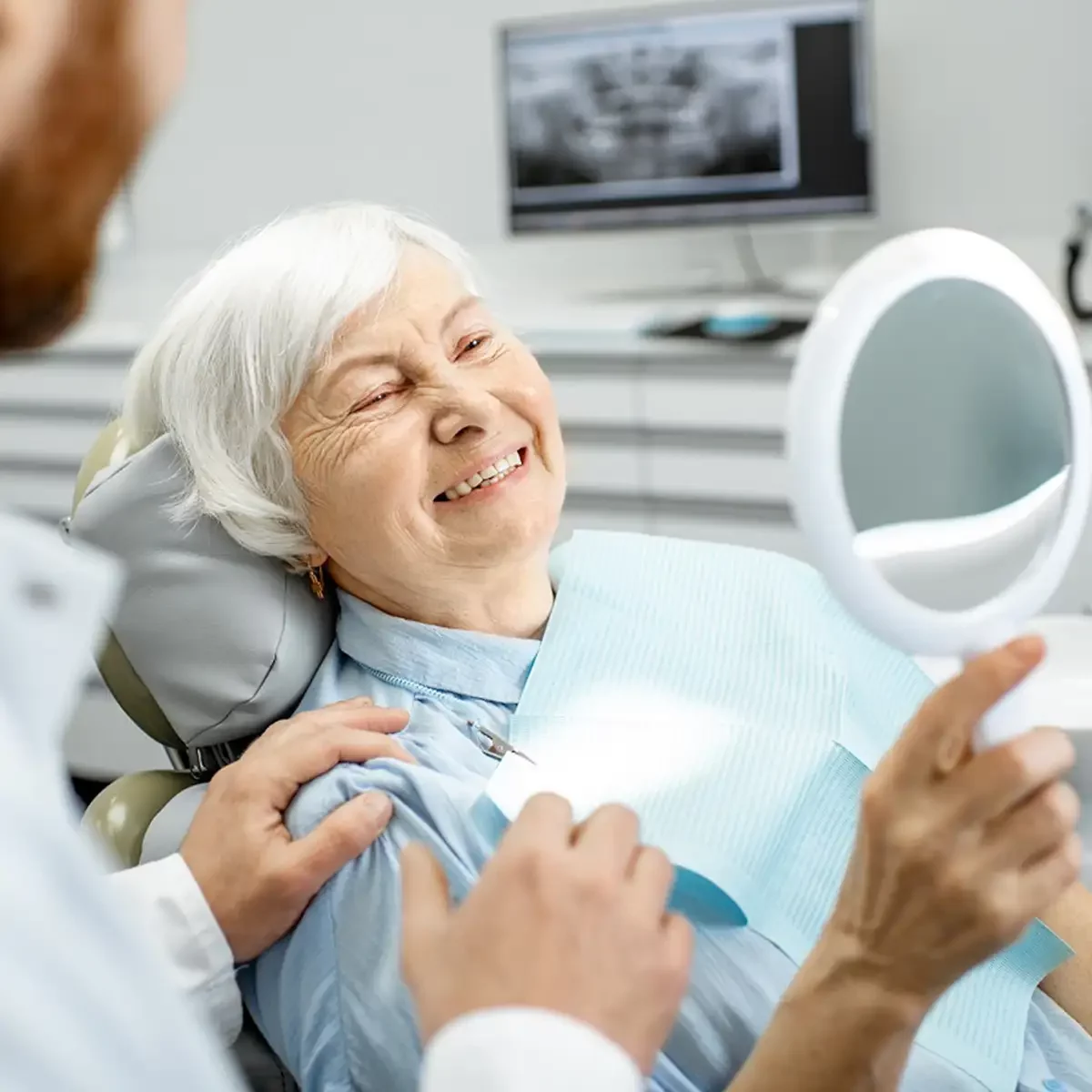 A woman with dentures smiles contently in a dentist chair, showcasing the importance of dental care