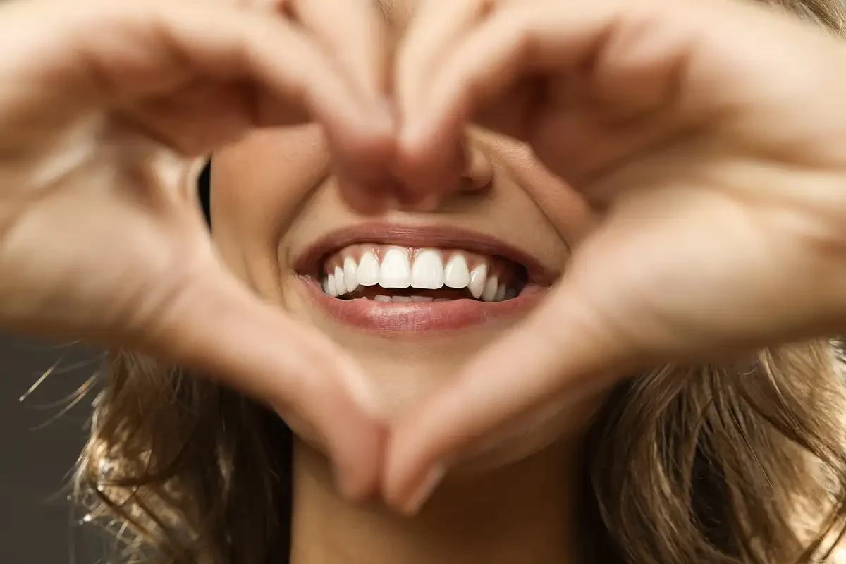 Woman making heart shape with hands showing her perfect teeth at Zara Dental Clinic