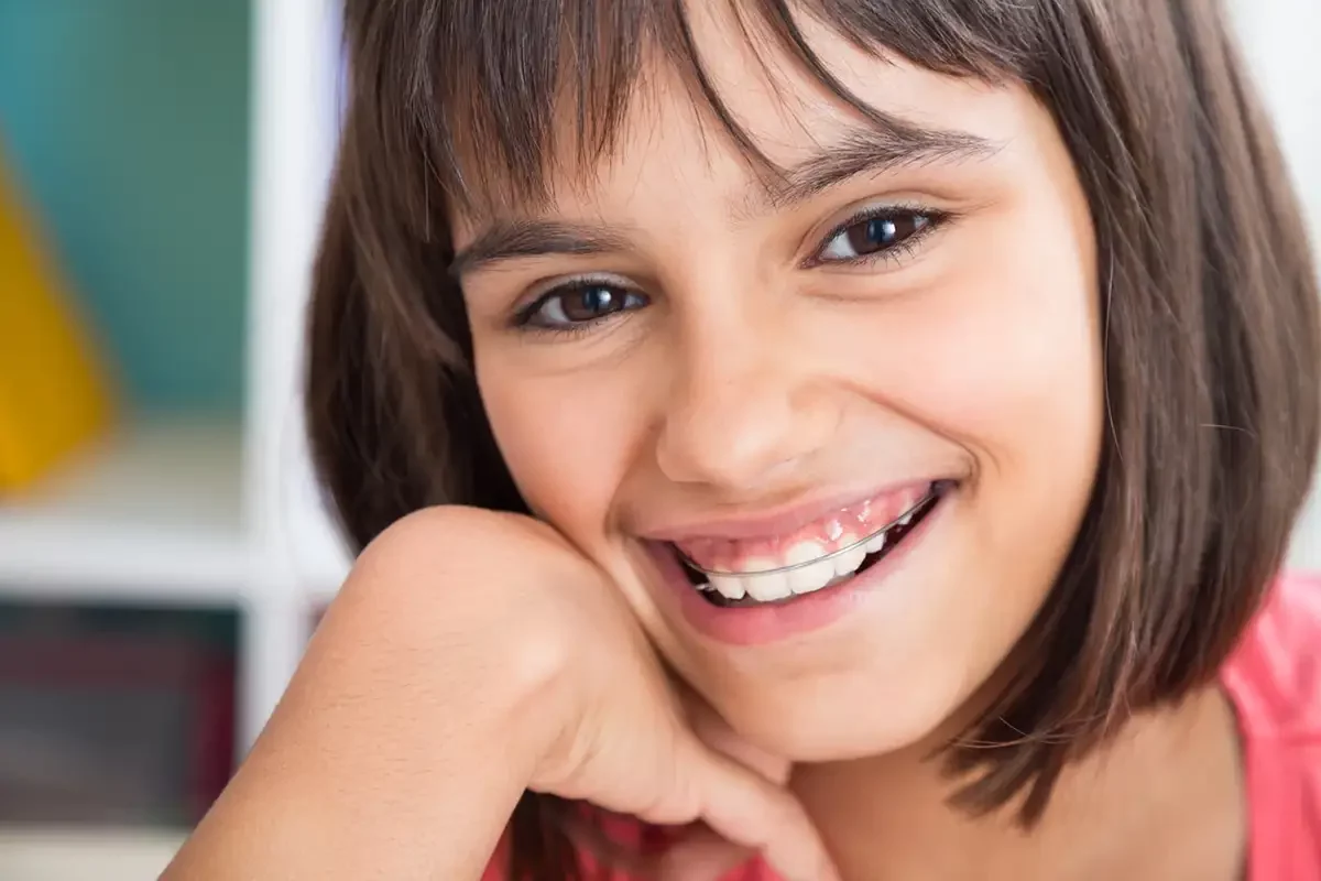 A young girl with retainers smiles happily while sitting at a table